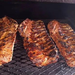 three steaks cooking on a grill