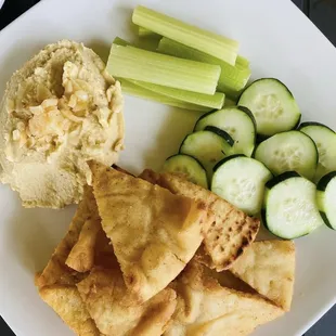 a plate of crackers, cucumbers, and hummus