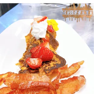 a plate of french toast with bacon and strawberries