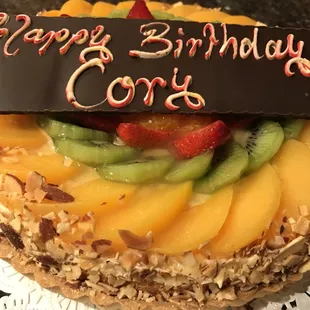 Fruit flan: glazed fruit on top of custard, yellow cake, and raspberry jam, inside a tart shell