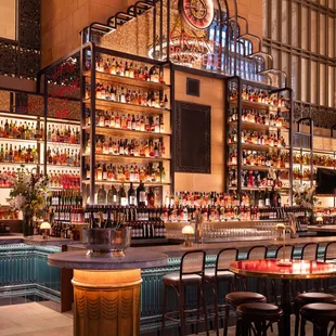 Past the main dining area, two windows frame a signature time piece with backlit bronze and glass shelving, drawing guests to the bar.
