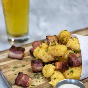 a bacon and shrimp sandwich on a cutting board next to a glass of beer