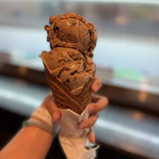 a hand holding a cone of chocolate ice cream
