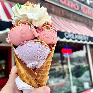 Taro &amp; strawberry ice cream with whipped cream and rainbow sprinkles in a waffle cone
