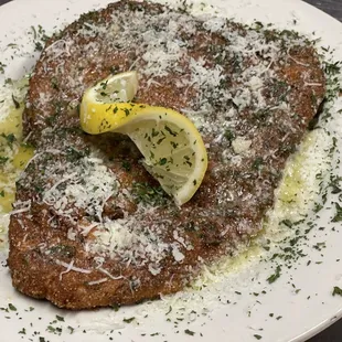 a piece of meat with parmesan cheese and a lemon wedge