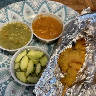 a chicken wrapped in foil with a side of dipping sauces