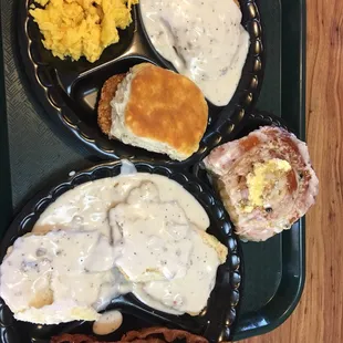 Biscuits and gravy, sinnamon roll topped with butter, chicken friend chicken, hash browns, scrambled eggs, bacon, and a biscuit.