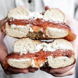 a person holding a bagel with cream cheese and bacon