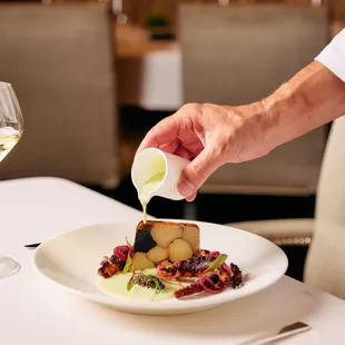 a person pouring white wine into a plate of food