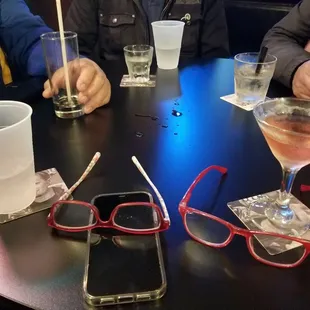 three people sitting at a table with drinks and cell phones