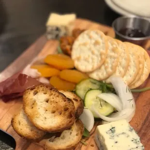 a wooden cutting board with cheese, crackers, and vegetables