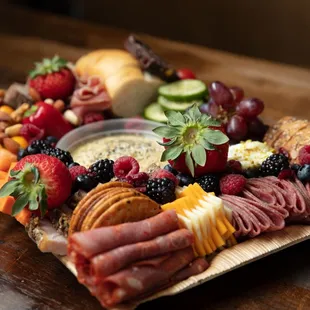 a platter of meat, cheese, fruit, and crackers
