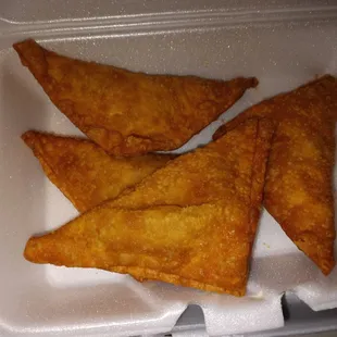 three fried triangles in a styrofoam container