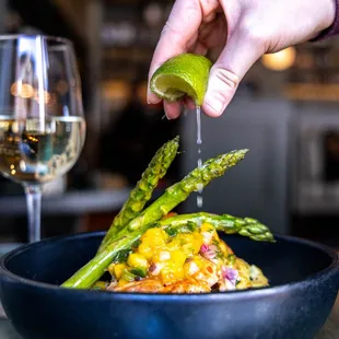 a person squeezing a lime over a bowl of asparagus