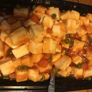 Tofu with vegetables. A very generous portion of soft tofu, cubed and topped with diced carrots and green peas with siracha.