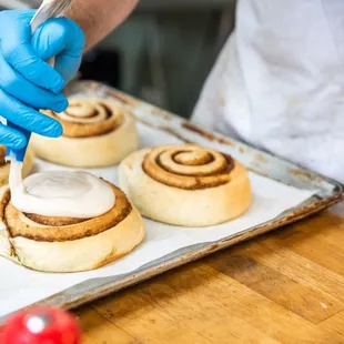 a person spreading icing on cinnamon rolls