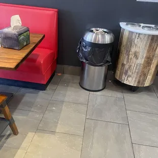 Food around the floor next to the garbage, including a visible slice of tomato. The place is a mess, like is running by high school kids