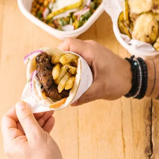 a person holding a pita with a salad in the background