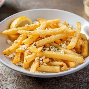 a bowl of french fries with lemon wedges