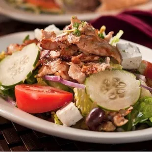 a salad with chicken, cucumbers, tomatoes, and onions