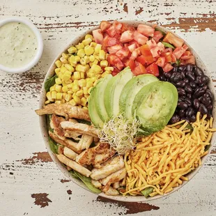 a bowl of salad with chicken, beans, tomatoes, avocado, corn, and black beans