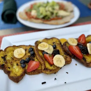a plate of french toast with strawberries, bananas, and blueberries