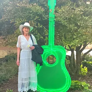 a woman in a white dress and hat standing next to a green guitar