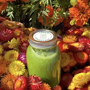 a jar of green smoothie surrounded by flowers