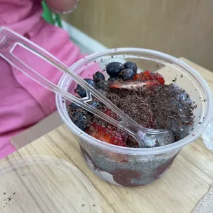 a woman in a pink shirt mixing a bowl of chocolate with strawberries, blueberries, and strawberries
