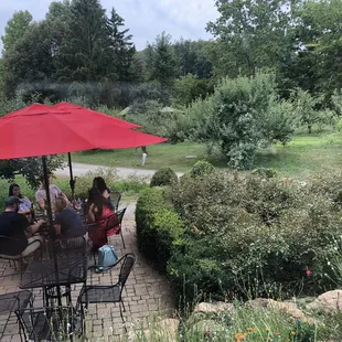 a group of people sitting at a table under a red umbrella
