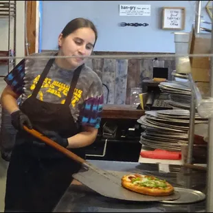 Gena takes my pizza out of the brick oven, after baking it for eight or so minutes.