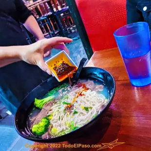 a person dipping sauce over a bowl of noodles