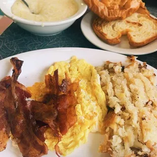 Grits, croissant, eggs, bacon, and hash browns