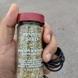 a hand holding a jar of fennel seed
