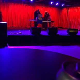 two people on stage with red curtains