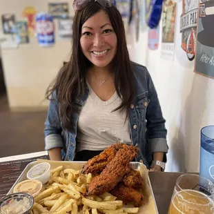 a woman sitting at a table with a plate of fried chicken and french fries