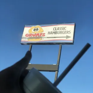 a hand holding a drink in front of a sign