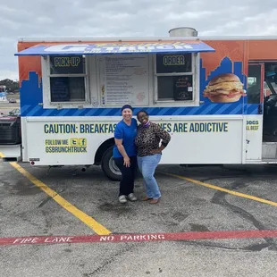 two people standing in front of a food truck
