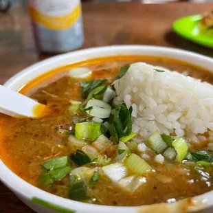a bowl of gumbo with rice and scallions