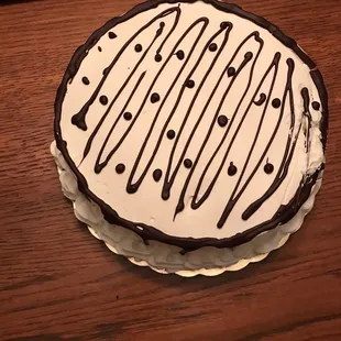 White cake with whipped cream frosting and chocolate ganache design. I caught the edge of the cake when I removed it from the box. ‍
