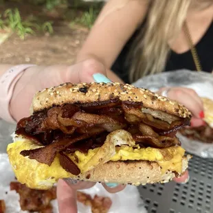 a person holding a sandwich with bacon and eggs