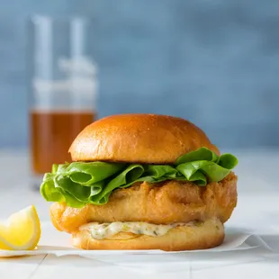 a chicken sandwich with lettuce and a lemon wedge