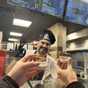 Two patrons holding falafel samples in front of the owner!