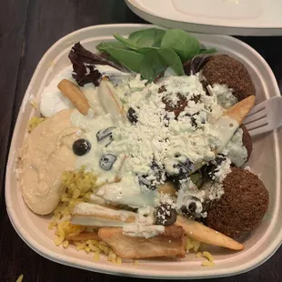 Bowl with rice, fries, falafel, tzatziki, black olives, hummus, mixed greens, and feta cheese