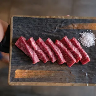 a person holding a cutting board with raw meat on it