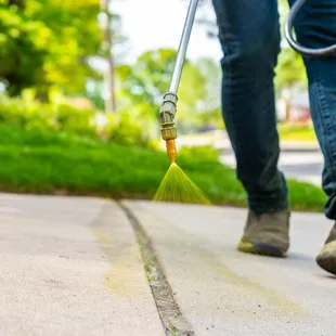 a person using a sprayer to clean a sidewalk