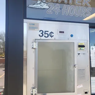 a vending machine in front of a water 24 hours sign