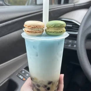  a hand holding a cup of iced tea with macarons on top