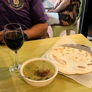 a man sitting at a table with a bowl of soup and a glass of wine