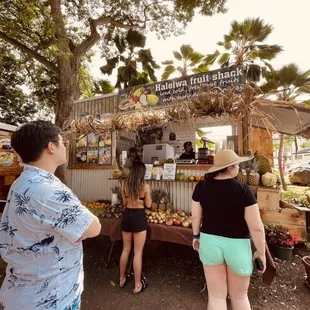 two people standing in front of a fruit stand